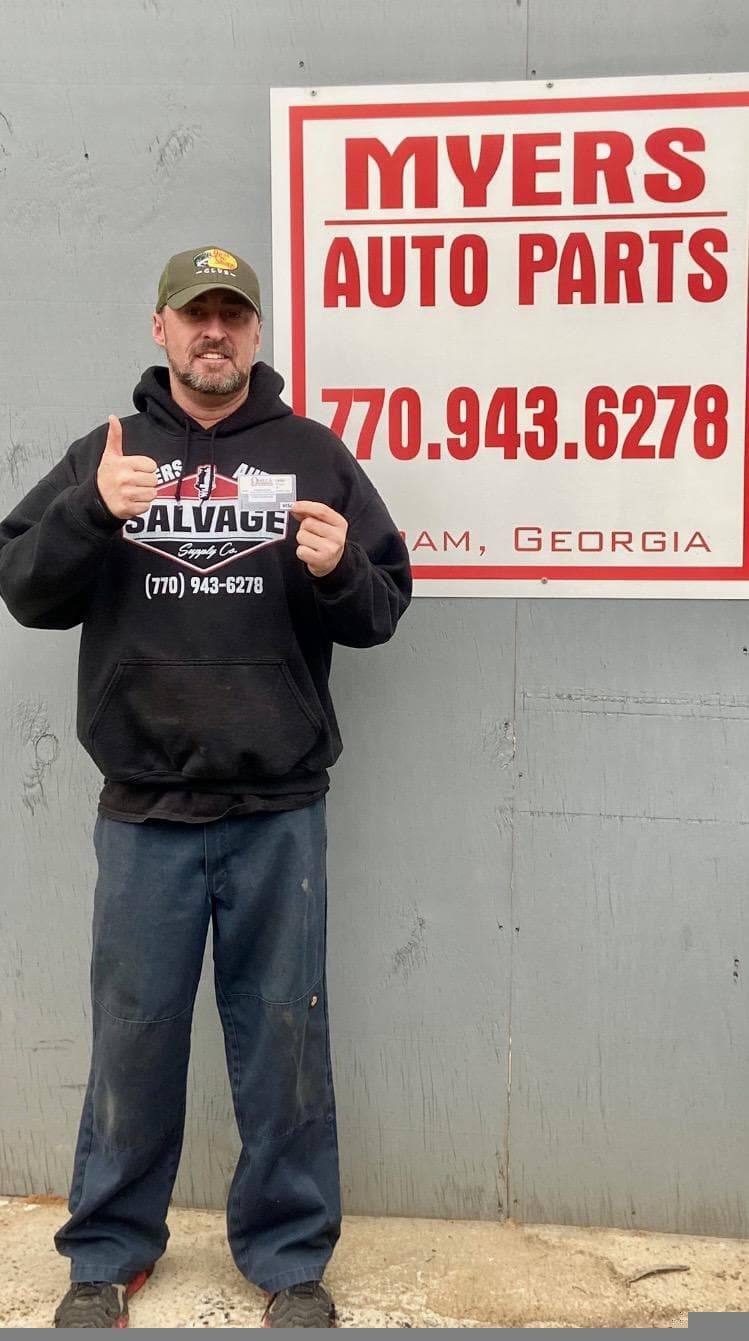Auto parts merchant with rewards card in front of business signage, Omega Rewards program